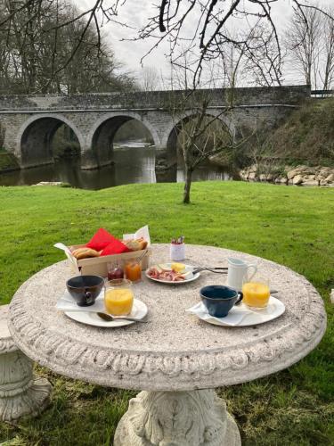 einen Steintisch mit Teller mit Lebensmitteln und Orangensaft in der Unterkunft Le Moulin De Bretigneul in Saint-Aubin-des-Landes