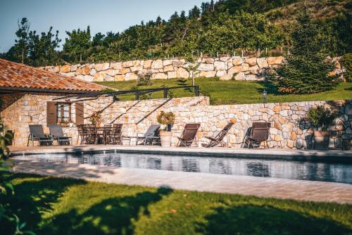 a swimming pool with chairs and a stone wall at La Ferme du Vallon by ExplorHome in Labatie-dʼAndaure