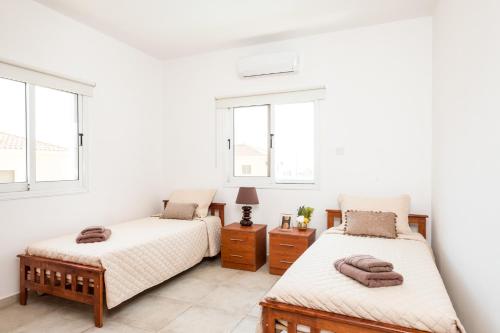 a bedroom with two beds and two windows at Voroklini Villa with Pool in Larnaka