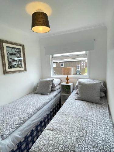 two beds in a room with a window at 93 Broadside Holiday Chalet near Broads & Beaches in Stalham