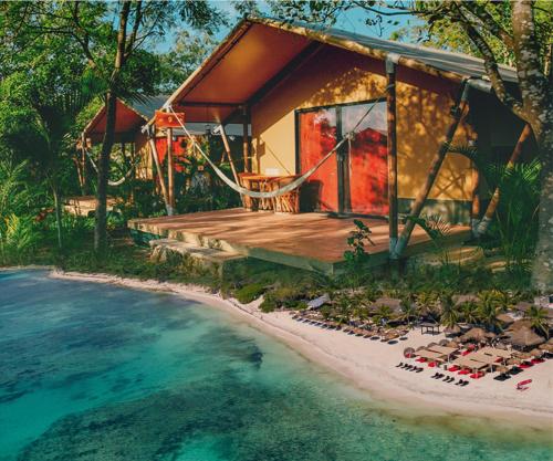 a house on the beach with a deck and the water at Serenity Authentic Glamping Tulum in Xpu Ha