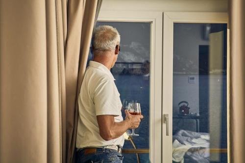 a man holding a glass of wine looking out a window at Hotel Paradiso Conca d'Oro in Nago-Torbole