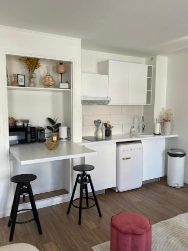 una cocina con armarios blancos y 2 taburetes. en Appartement Entre Paris et Disney en Ozoir-la-Ferrière