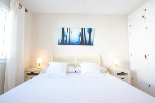 Un dormitorio blanco con una gran cama blanca con dos lámparas. en Los Lances Playa en primera linea, en Tarifa