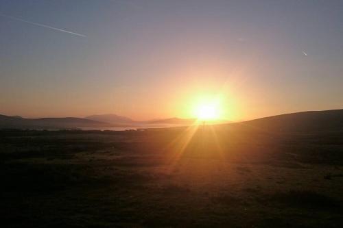 a sunset in a field with the sun setting in the sky at Skellig View Harbour View Sunrise Apartment in Portmagee