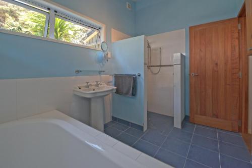 La salle de bains est pourvue d'une baignoire, d'un lavabo et d'une fenêtre. dans l'établissement Frosty's Retreat - Great Barrier Island Home, à Tryphena