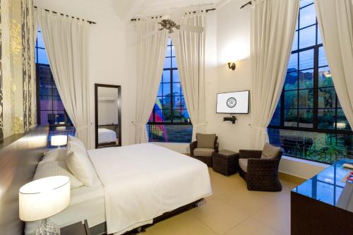 a bedroom with a white bed and two windows at Hotel Republicano 1910 in Girardot