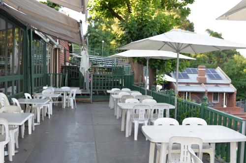 Mundaring的住宿－Mundaring Weir Hotel，餐厅外的一排白色桌子和遮阳伞