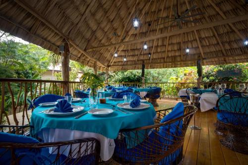 a dining room with blue tables and chairs under a roof at Mariposa Belize Beach Resort in Placencia Village