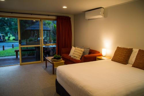 a bedroom with a bed and a chair and a window at Hahei Beach Resort in Hahei