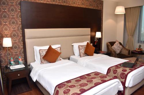 two beds in a hotel room with white sheets at Lords Plaza Surat in Surat