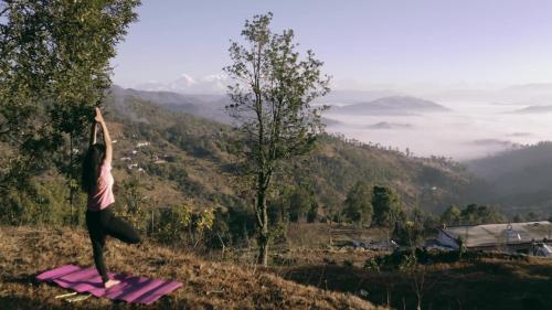 a woman doing a yoga pose on top of a mountain at Nayalap - Rural Himalayan Glamping in Shitlakhet