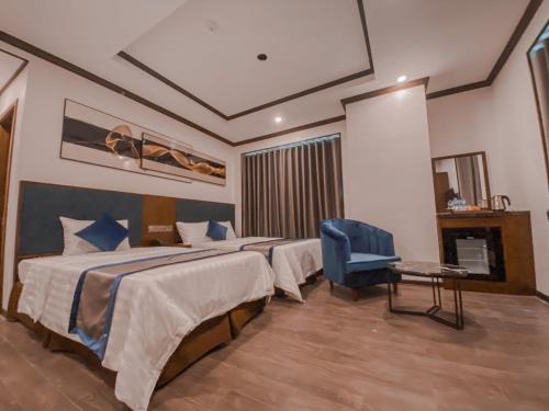 een hotelkamer met 2 bedden en een blauwe stoel bij Kingdom Hotel Cua Lo in Cửa Lô