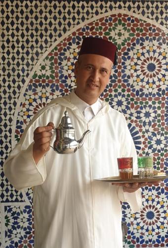 a chef holding a tray with a tea kettle and drinks at Riad TANJIL in Casablanca