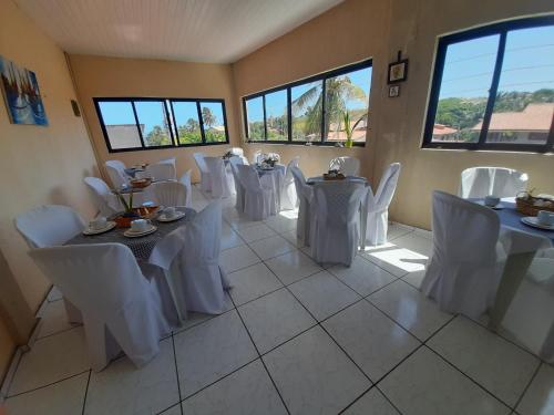 una habitación con mesas blancas, sillas blancas y registradora en Pousada Maria Brasil, en Paracuru