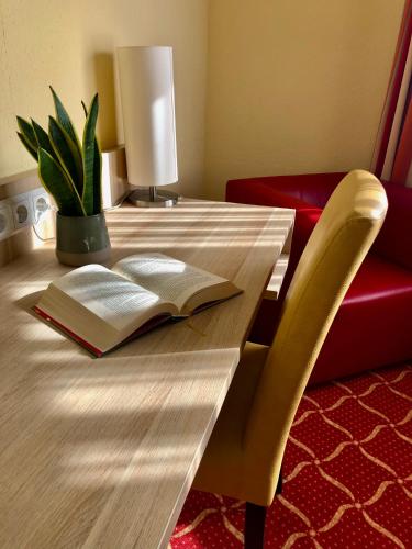 a book on a wooden table with a lamp and a plant at Montana Hotel Köln-Bonn Airport in Troisdorf