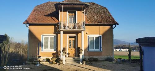 ein kleines gelbes Haus mit einem Balkon und einer Veranda in der Unterkunft La Maison Fleur de Frangipanier in Saint-Genix-sur-Guiers