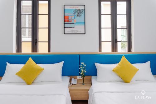 two beds with yellow pillows in a room with windows at La Playa Ha Long Hotel in Ha Long