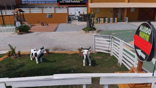 Arraial do Cabo – Subuai Village - Aluguel Econômico في أرايال دو كابو: بقرتان وهميتان واقفتان بجانب سياج أبيض