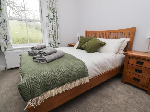a bedroom with a bed with a green blanket and a window at 1 Hull House Cottage in Skipton