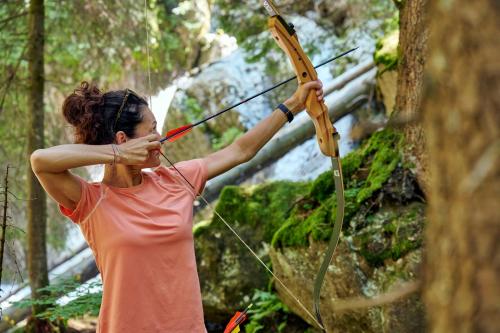 a woman holding a bow and arrow in the woods at Woodpecker Chalets in Klösterle am Arlberg