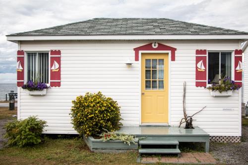 a small white house with a yellow door and flowers at Les Cabines du Phare in Rimouski