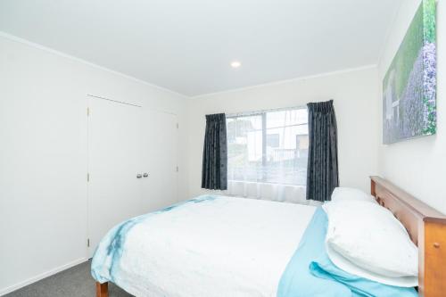 a white bedroom with a bed and a window at Family Home on Robert St in Raglan