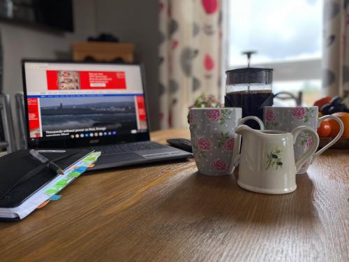 a table with two coffee cups and a laptop computer at Mountain View Cottage - Style, Calm & Scenery EV Friendly Zappi in Ray
