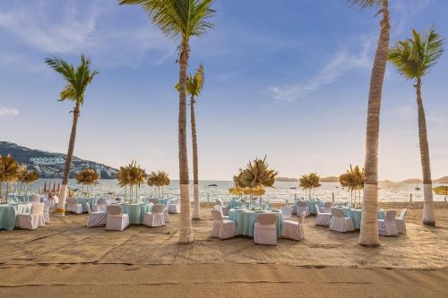 a group of tables and chairs on a beach with palm trees at Copacabana Beach Hotel Acapulco in Acapulco