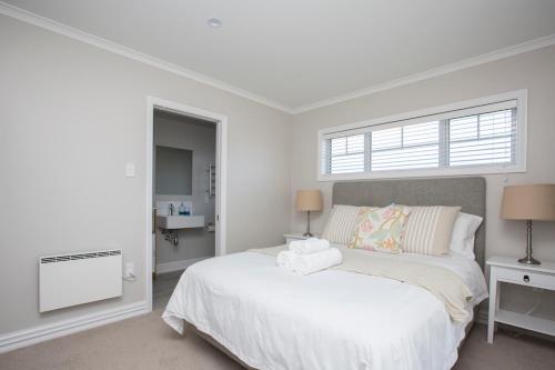 a white bedroom with a bed and a window at The Boathouse in One Tree Point