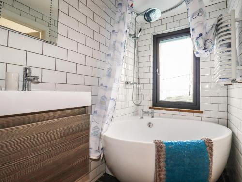 Un baño con bañera, lavabo y ventana. en Blue Bay Beach House, en Newquay