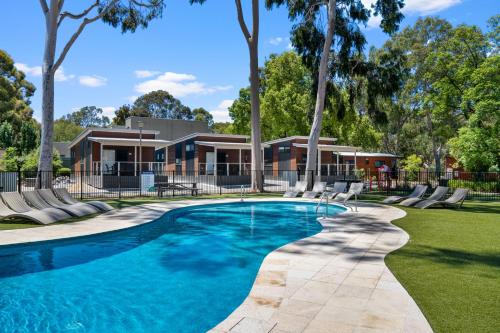 a swimming pool in front of a house with trees at Levi Adelaide Holiday Park in Adelaide
