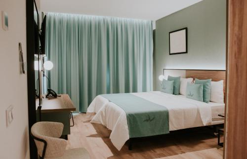 a bedroom with a bed with green curtains and a desk at Hotel Catalina Plaza Sostenible in Las Palmas de Gran Canaria