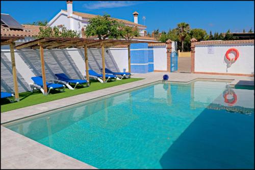 a swimming pool with blue chairs and an umbrella at Bungalow La Roa V in Conil de la Frontera