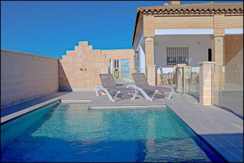 una piscina con due sedie accanto a una casa di Chalet Peñuelas con piscina a Conil de la Frontera