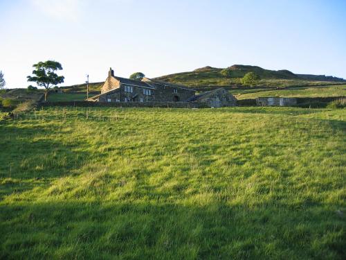 a large grassy field with a house on a hill at Rake Hey Farm in Todmorden
