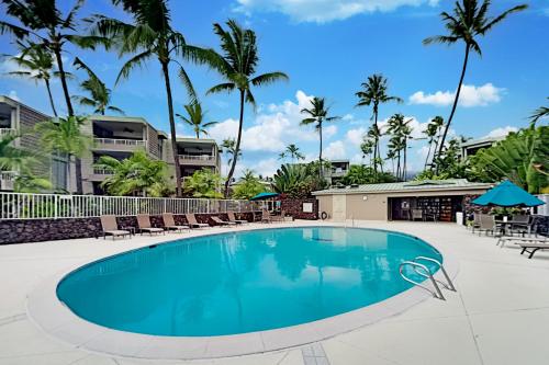 a swimming pool with chairs and palm trees at Alii Villas 201 in Kailua-Kona