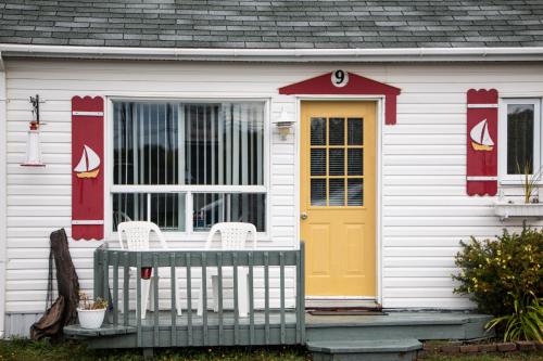 a white house with a yellow door and two chairs at Les Cabines du Phare in Rimouski