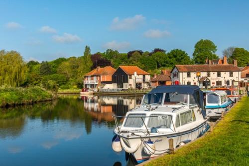 a boat is docked on a river next to houses at Stylish 2 bed apartment next to the Norfolk Broads in Coltishall