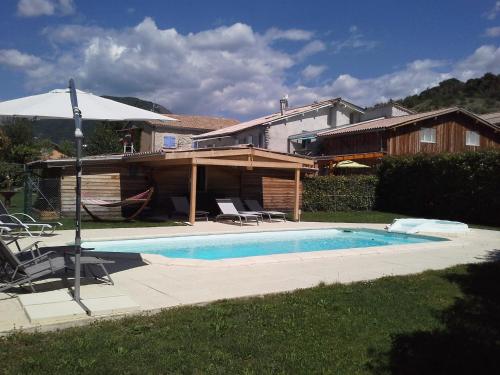 a swimming pool with an umbrella next to a house at Chambres d'hôtes La Dorgisane in Venterol