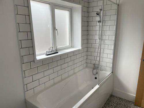baño blanco con bañera y ventana en STOP at Pendarvis, Stone throw from beach!, en Port Talbot
