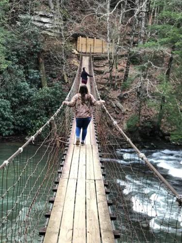 a woman walking across a suspension bridge over a river at Gas fireplace, firepit, and cedar Adirondack chair in Spencer