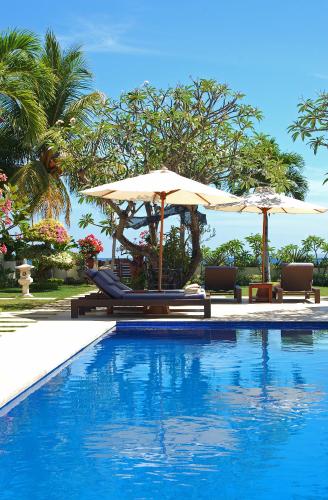 a swimming pool with two umbrellas and two chairs at Frangipani Beach Hotel in Lovina