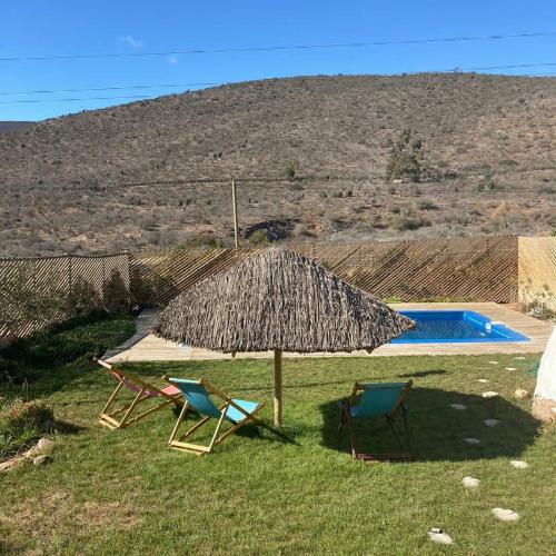 two chairs and a straw umbrella and a swimming pool at Ecodomos La Tongoycilla in Guanaqueros