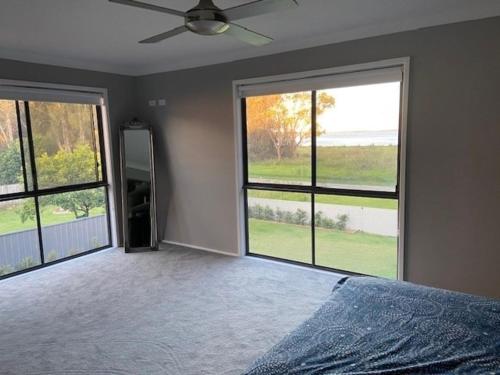 a bedroom with two large windows and a bed at Lakefront Holiday Home in Berkeley Vale