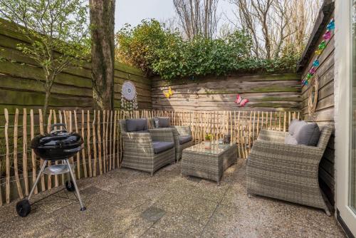 eine Terrasse mit Korbstühlen, einem Grill und einem Zaun in der Unterkunft BeachHouse Oase aan Zee in Noordwijk