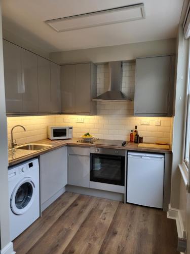 a kitchen with white cabinets and a washer and dryer at 1 Bed Apartment Russell Square in London