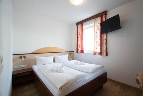 a bedroom with a bed with white sheets and a window at Hotel-Gasthof Andreas in Obertilliach