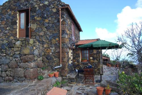 una casa de piedra con una persona sentada bajo un paraguas en Casa Abuela Estebana, en Isora