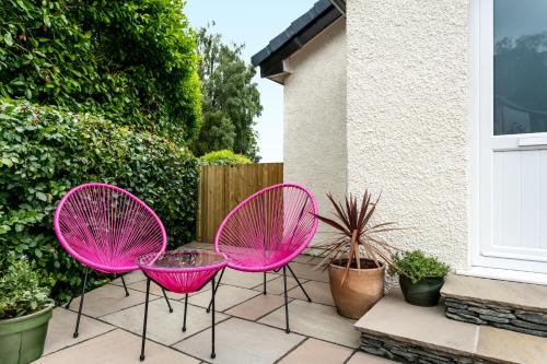 three pink chairs sitting on a patio next to a house at Stylish Flat - Bowness centre with parking in Bowness-on-Windermere